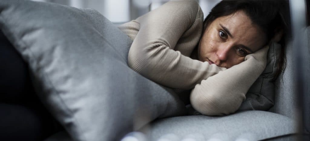 Imagem mostra uma mulher deprimida, deitada sobre a cama com um rosto triste