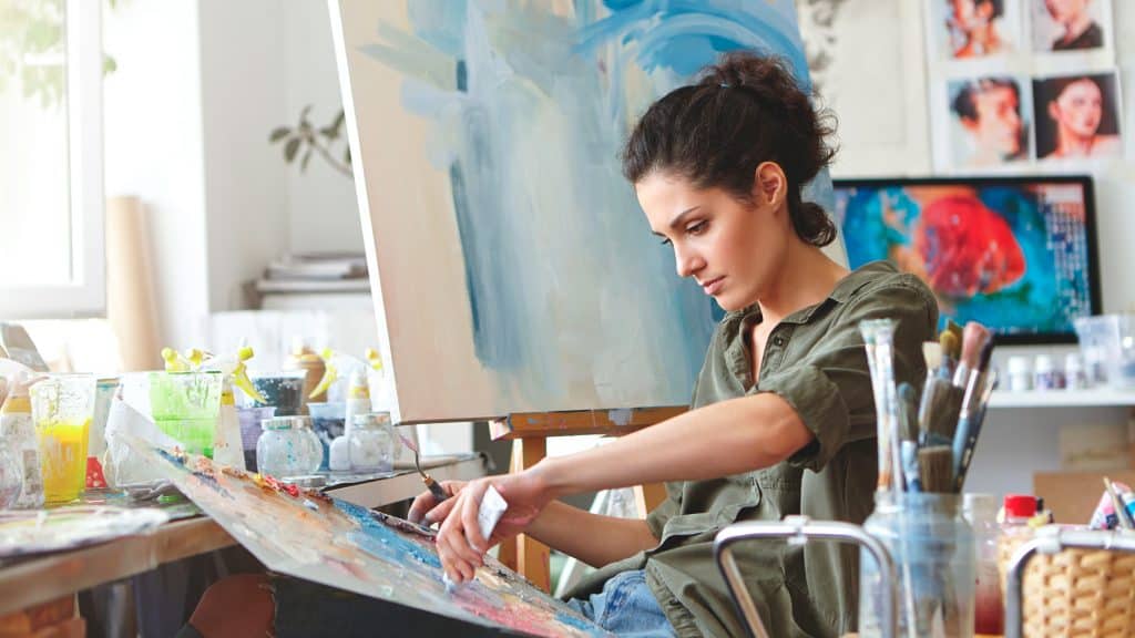 Mulher mexendo em paleta de cores para continuar pintando quadro em seu ateliê