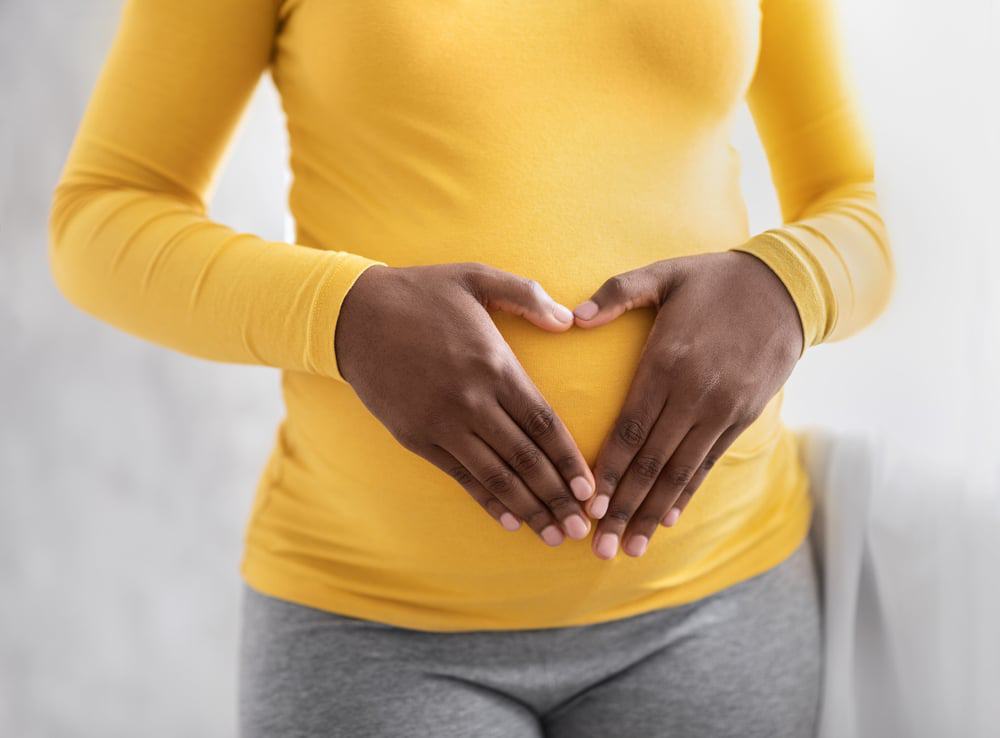 mulher negra com as mãos em formato de coração sobre a barriga