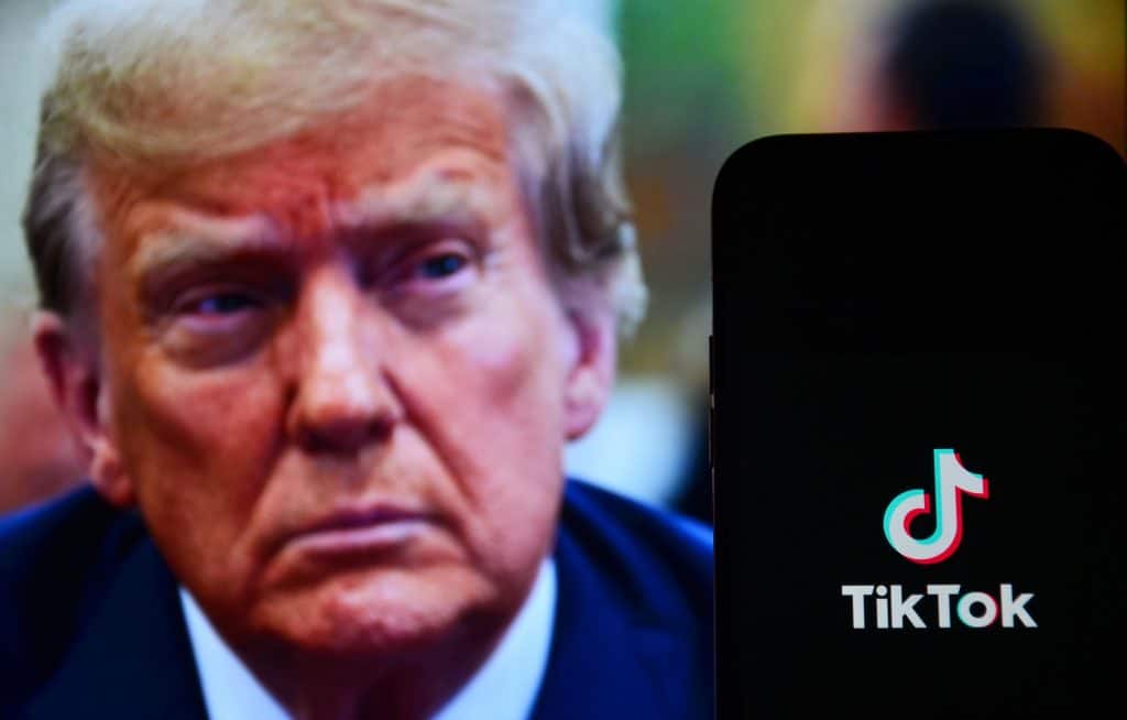 Ao fundo, rosto de onald Trump desfocado; à frente, logo do TikTok em um smartphone