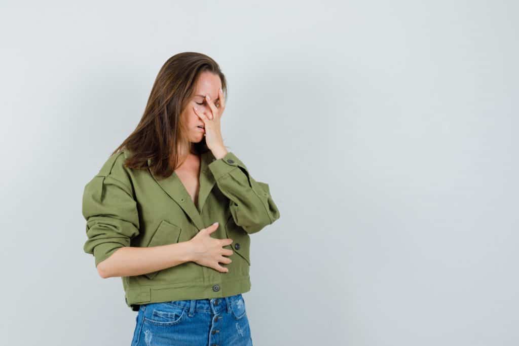 mulher com blusa verde, mão na barriga e outra mão no rosto