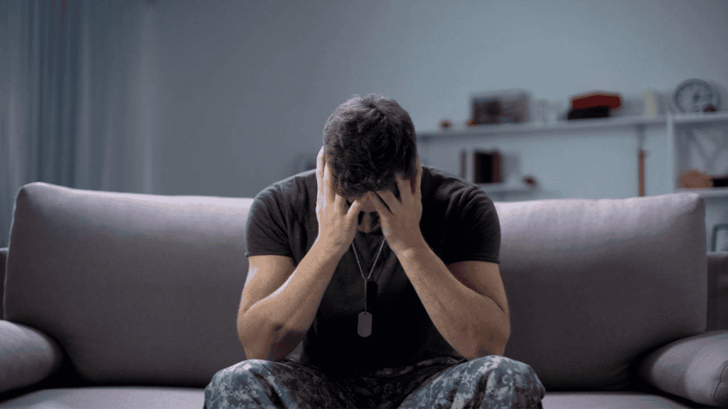 imagem mostra um homem sentado no sofá com as mãos apoiadas no rosto, triste