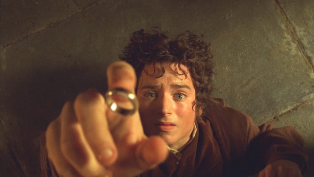 imagem mostra um close-up do personagem frodo pegando um anel no filme O SENHOR DOS ANÉIS