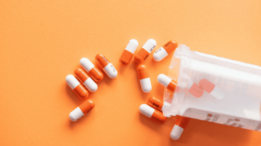 imagem mostra um frasco plástico sobre uma tela laranja, despejando várias unidades de pílulas medicamentosas