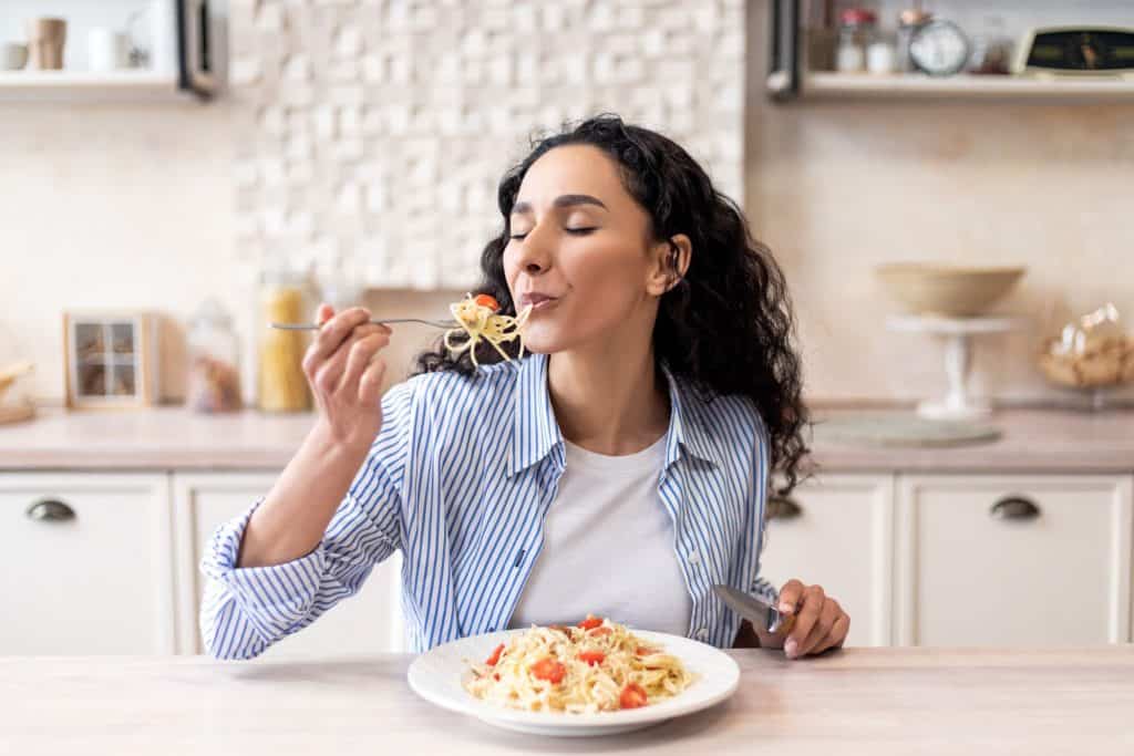 imagem mostra uma mulher aproveitando cada momento de sua refeição: macarronada
