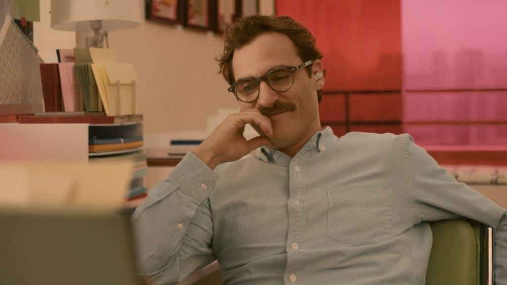 homem de bigode sentado em um soga com a mão no rosto e sorrindo