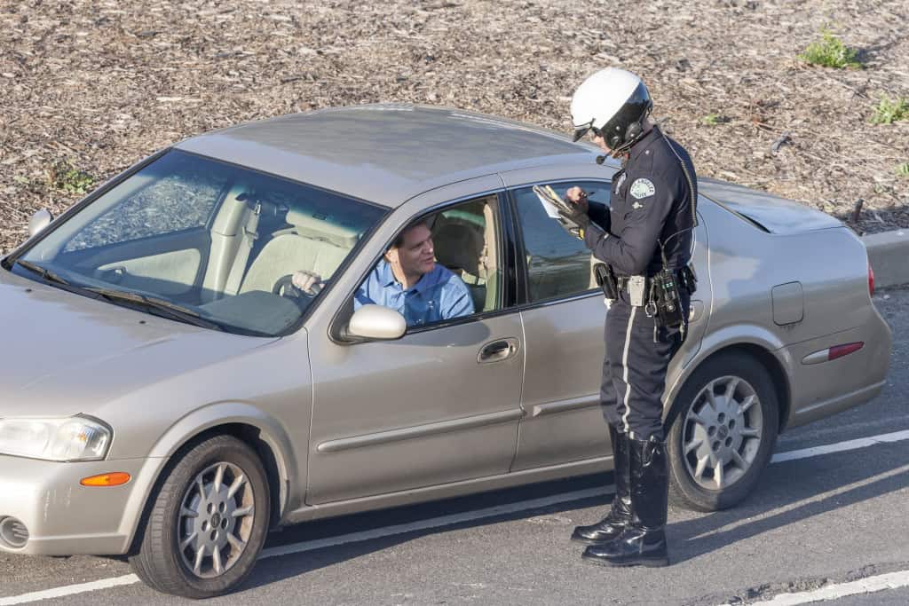 Imagem mostra policial de trânsito aplicando multa ao motorista de carro