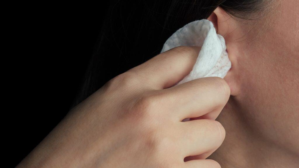 Mulher limpando o ouvido com o auxílio de uma toalha