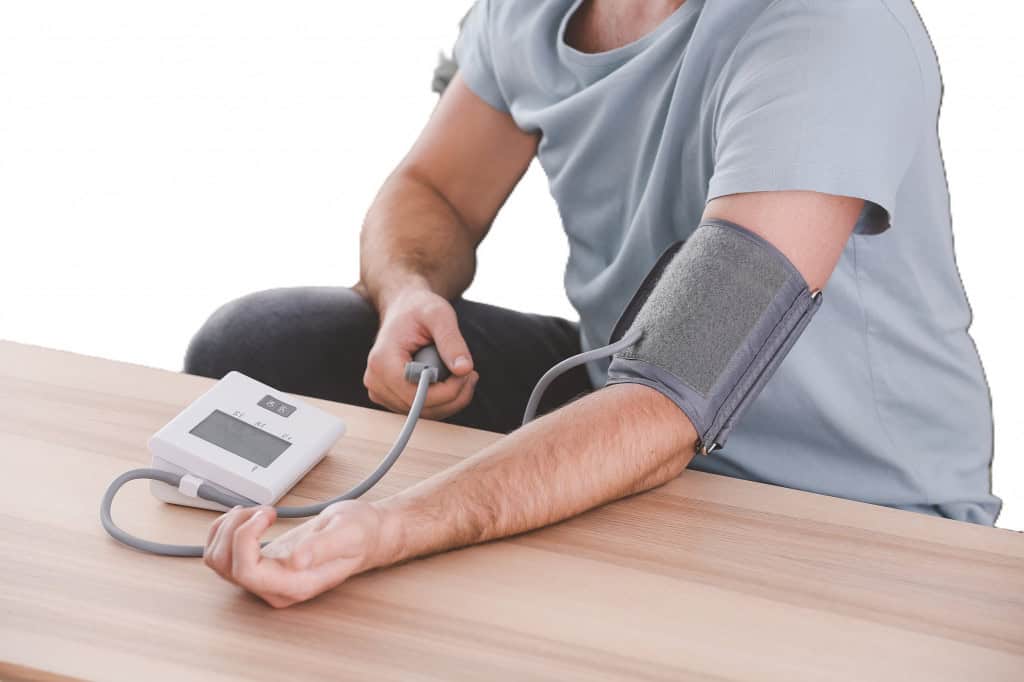 Pessoa medindo a pressão arterial em casa com aparelho digital no braço