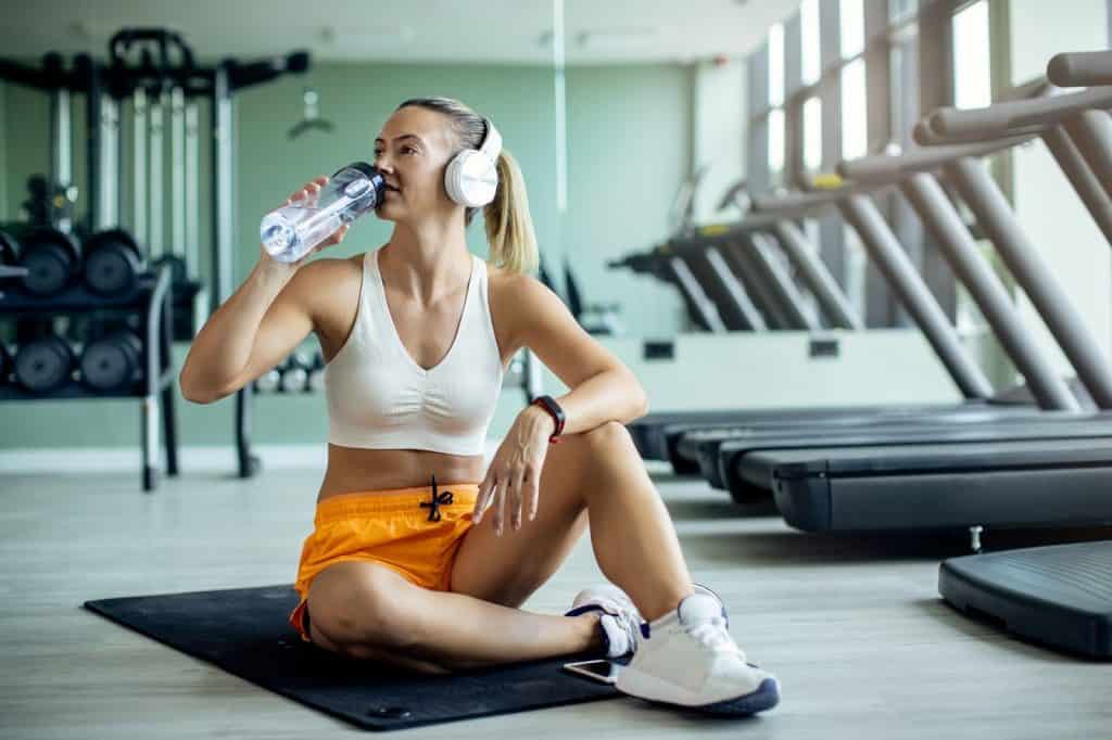 Mulher atlética bebendo água no chão do ginásio 