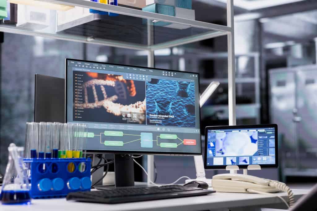 Laboratório de pesquisa com computadores exibindo análises de DNA e equipamentos usados no desenvolvimento de novas tecnologias em saúde.